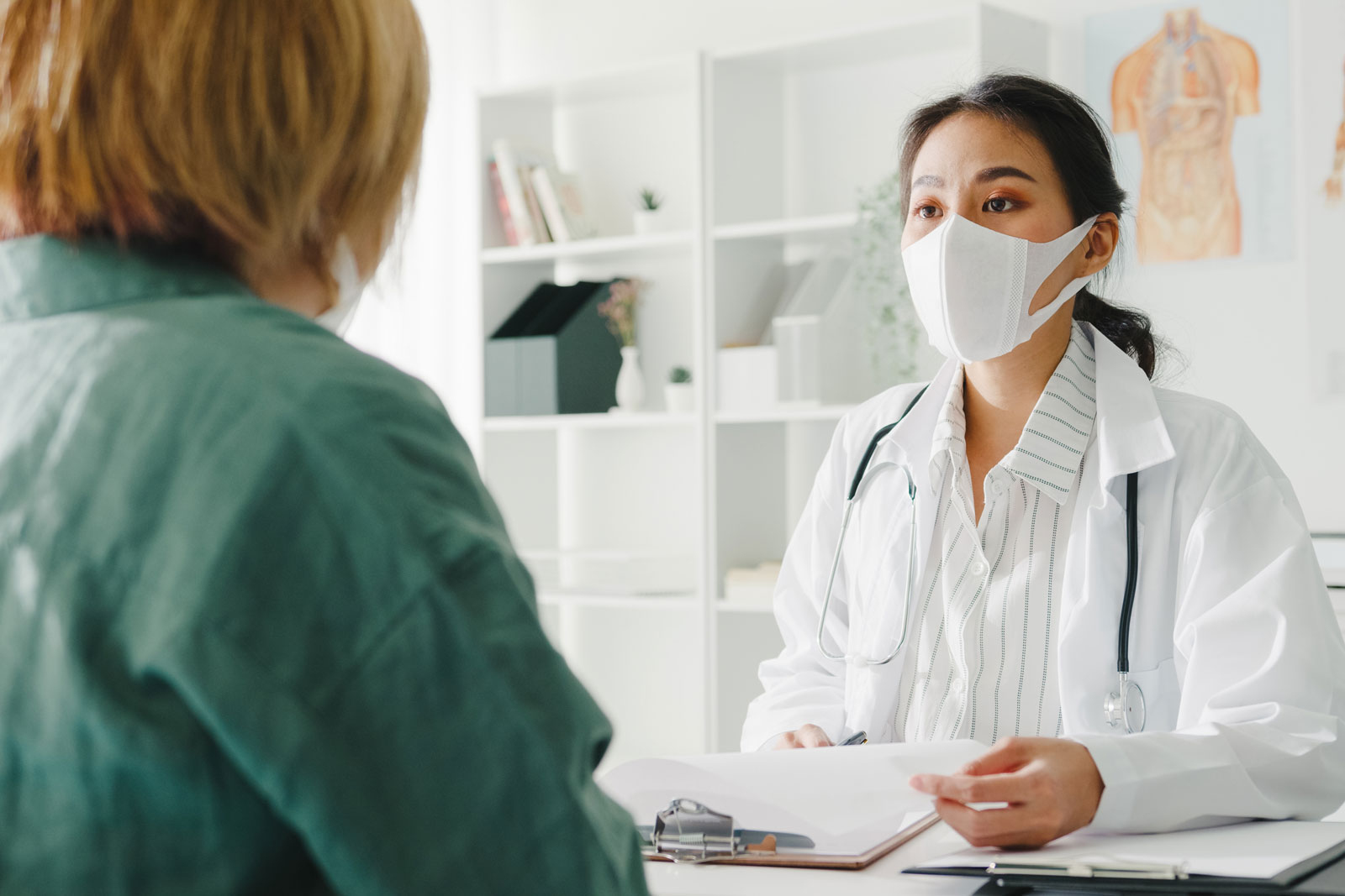 Young asian lady doctor wearing protective mask using clipboard discussing results